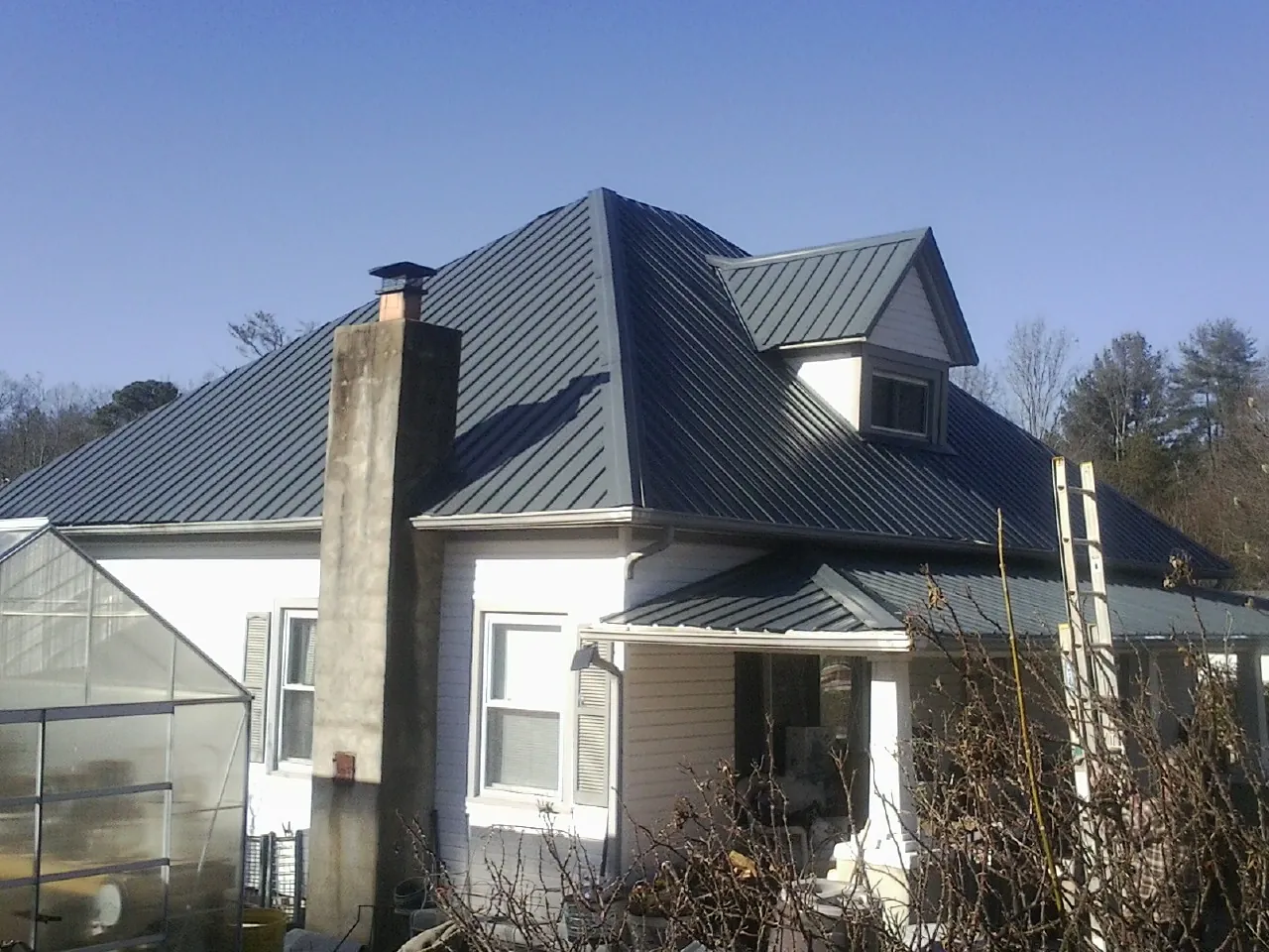 Dark blue standing seam metal roof on a white farmhouse with dormer — Slate & Tile Roof Repair by Roofing Brothers in Williams